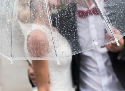 The bride & groom getting rained on, but they have an umbrella