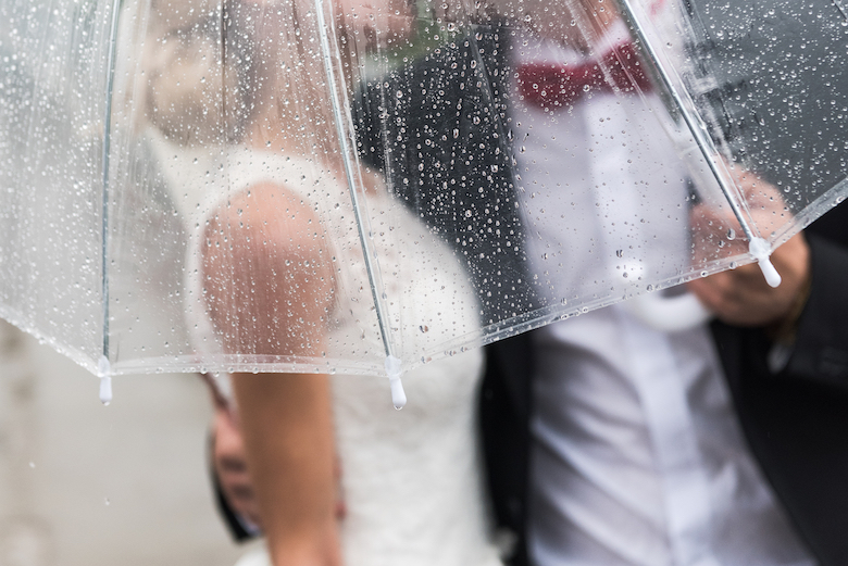 The bride & groom getting rained on, but they have an umbrella