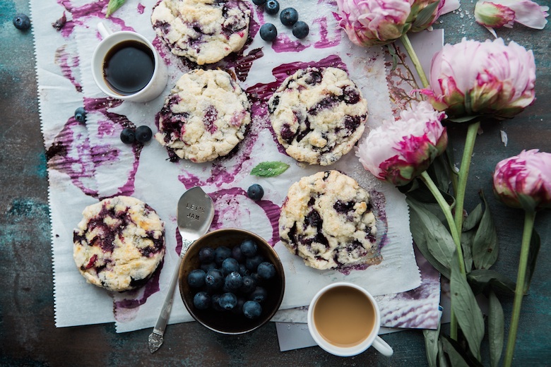 blueberry cookies and fruit spread out on a table, next to some pink purple flowers