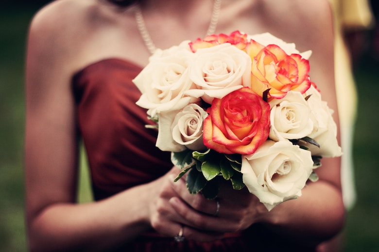 a bridesmaid holding a white and orange wedding bouquet