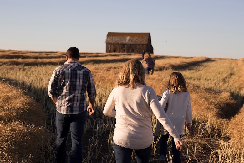 Family walking across a country pasture towards a wooden house