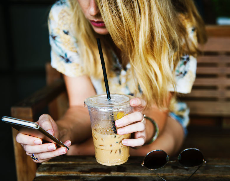 girl texting on her phone with one hand, iced coffee in the other