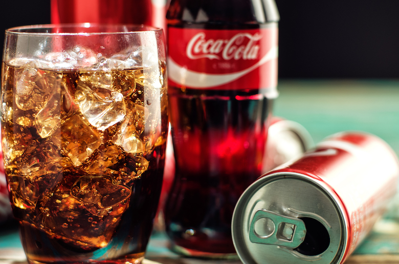 coca cola poured out into a glass, empty can and coke bottles