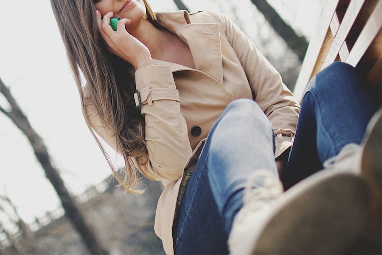 Smiling young woman in a tan coat talking on the phone