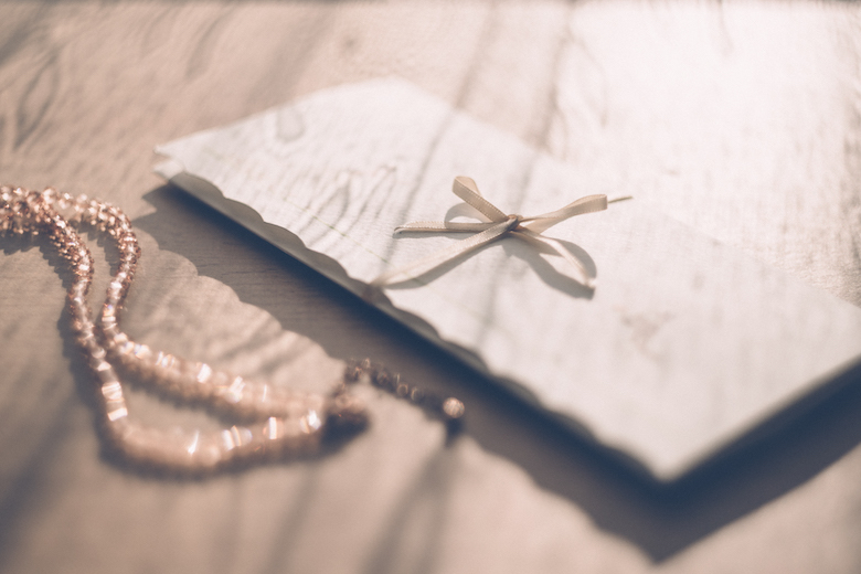 a letter tied with a nice bow, next to a necklace, wooden background
