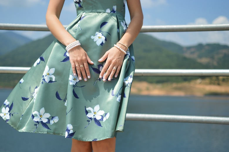 Young woman in a teal floral dress, standing on the hull of a ship, emphasis on hands and dress