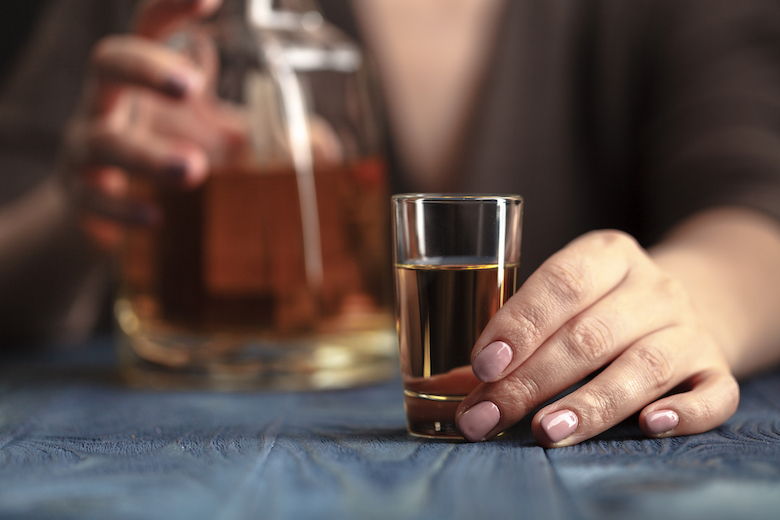 Woman's hand holding a bottle of whiskey & a whiskey shot
