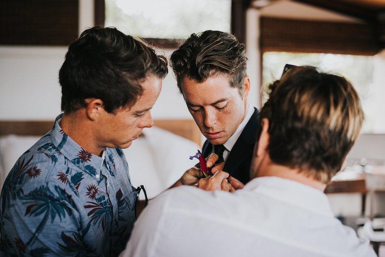 brother puts a boutonniere on his brother's suit at a tropical wedding