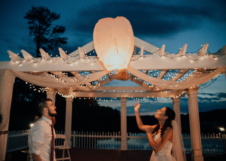 Bride and groom send a glowing lantern off into the night sky at their wedding venue