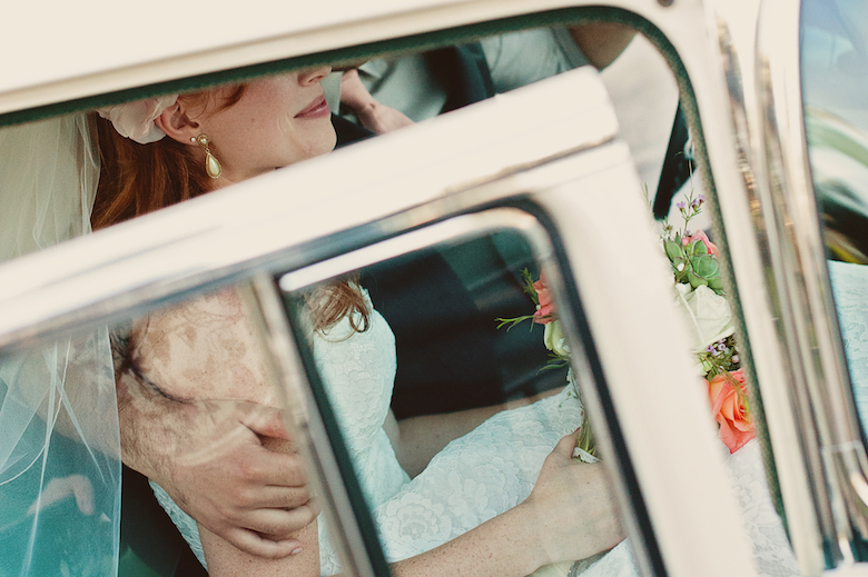 bride sitting in a beige car, groom's arm around her back, close up