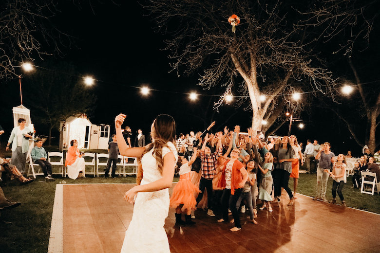 Bride throwing a flower bouquet into the air at an outdoor night wedding