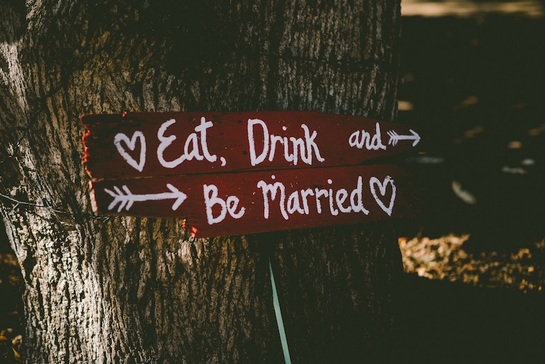 wooden wedding sign that says eat, drink, and be married, posted to a tree