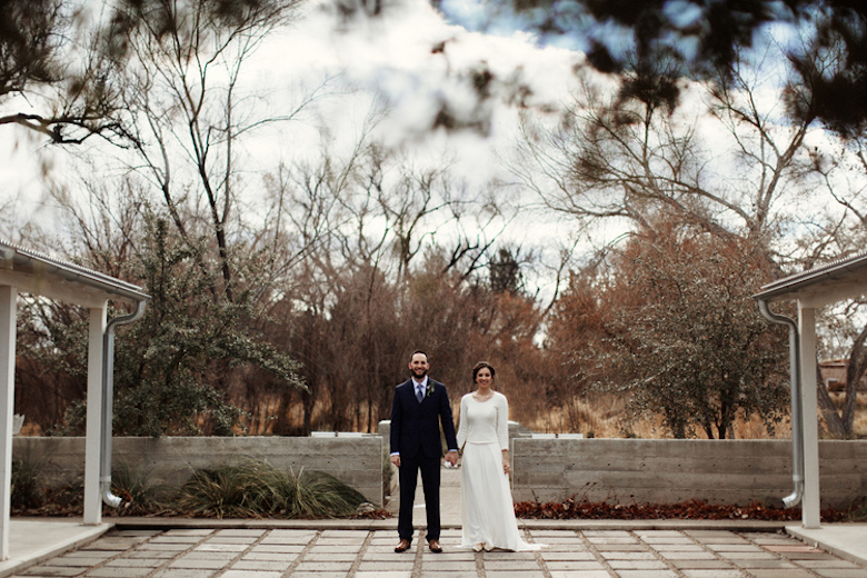 bride and groom standing outside posing for a photo, clearly winter with bare deciduous trees in the background