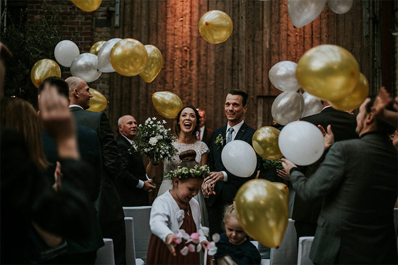 bride and groom smiling through a cloud of gold and white balloons