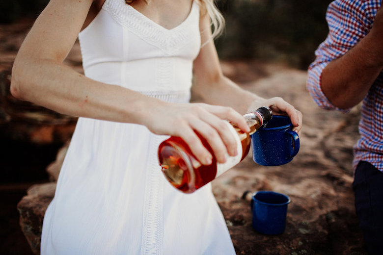 outdoor wedding photoshoot, bride pouring whiskey into a glass next to her husband