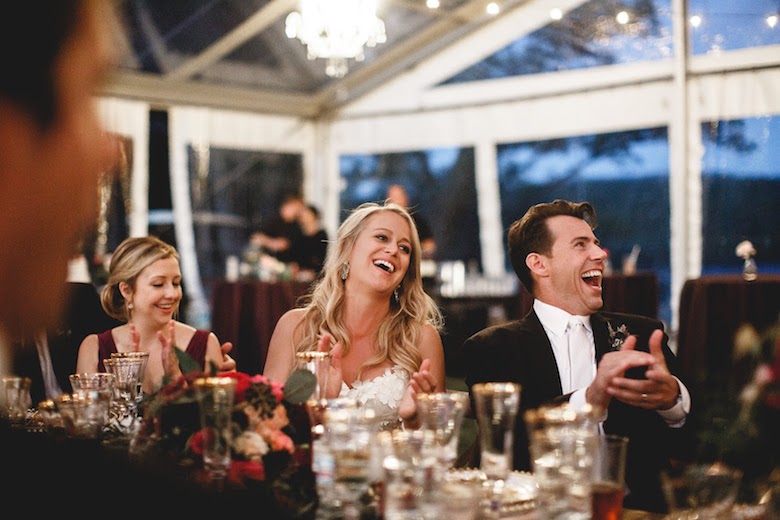 bride and groom laughing robustly at their indoor wedding, windows show it's dark outside