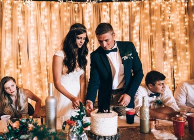 couple cutting cake against a glimmering light strings nude color chiffon backdrop