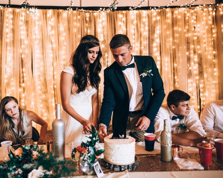 couple cutting cake against a glimmering light strings nude color chiffon backdrop