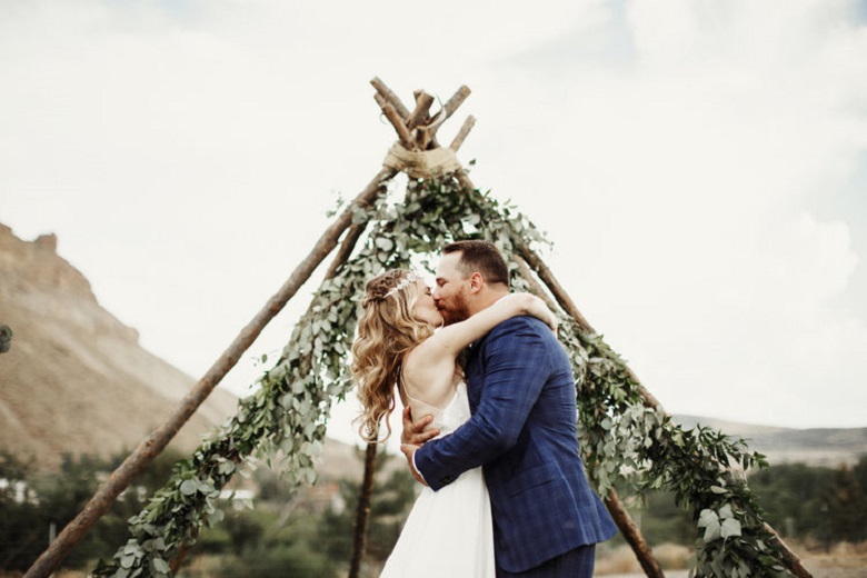 bride and groom kissing under a birch branch teepee ceremony marker