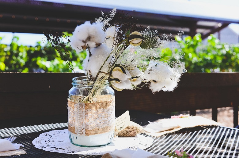 vintage mason jar wedding centerpiece with cotton flowers surrounded by burlap cloth