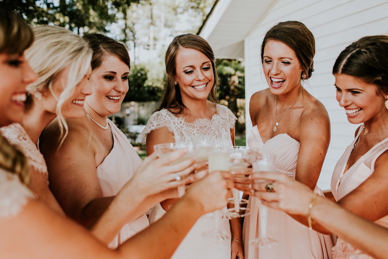 bride and bridesmaids enjoying a nice toast with champagne, wearing peach-colored bridesmaid dresses