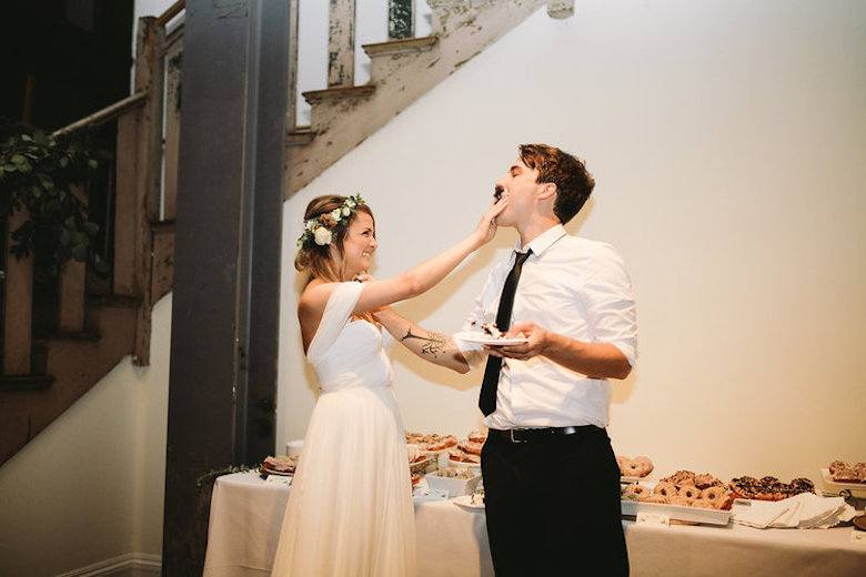 young bride pushing chocolate wedding cake into her husband's mouth