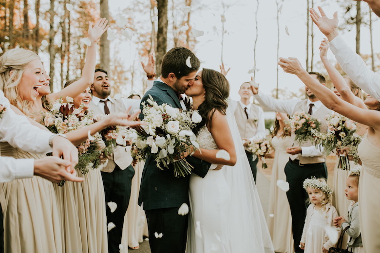 happy newlyweds kissing at the altar, outdoor wedding, white flowers, cheering audience