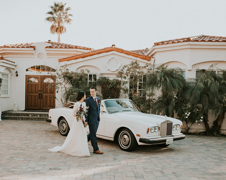 young bride and groom in front of a classic white car in front of a white house, tile roof