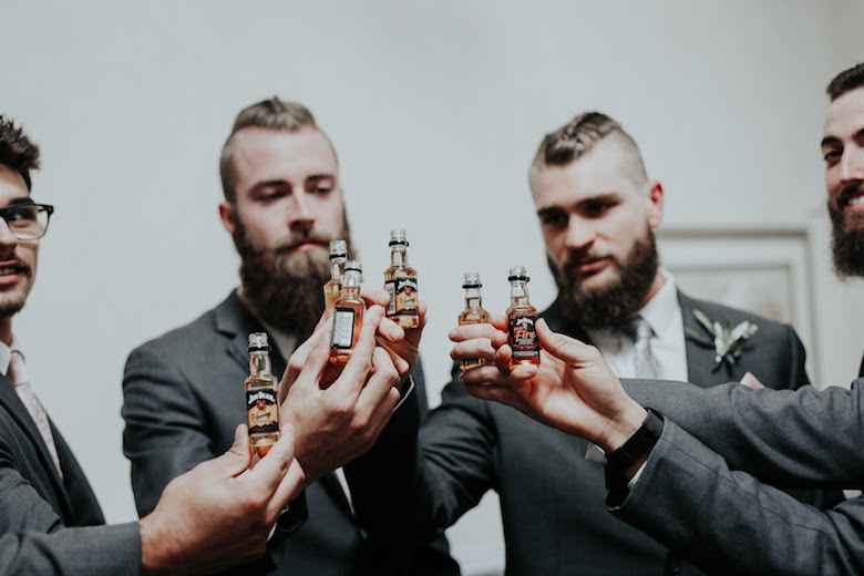 bearded groomsmen enjoy mini bottles of Jack Daniel's before a wedding, cheers!