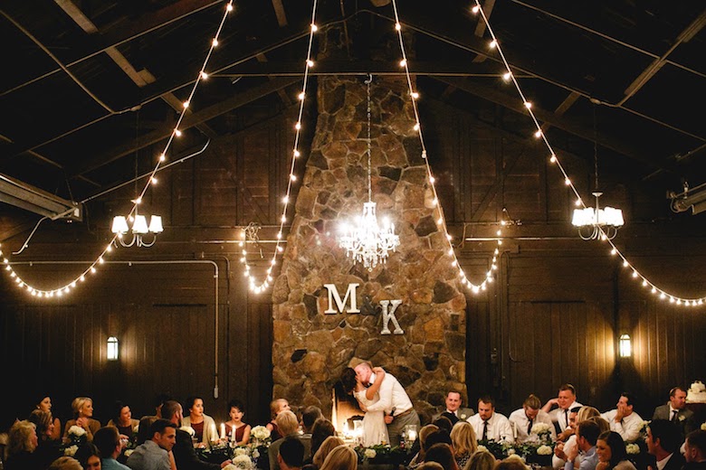 romantic indoor wedding, bride kisses the groom, lovely lights stringed across the ceiling