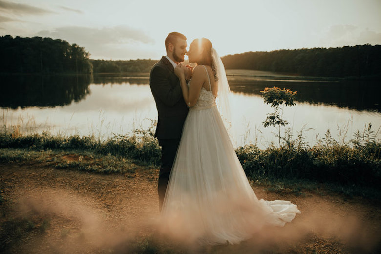 bride and groom embracing in the sunset next to a lake