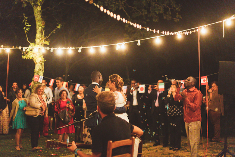 young groom and bride dance in the romantic lighting of an outdoor wedding as a solo guitar player serenades them