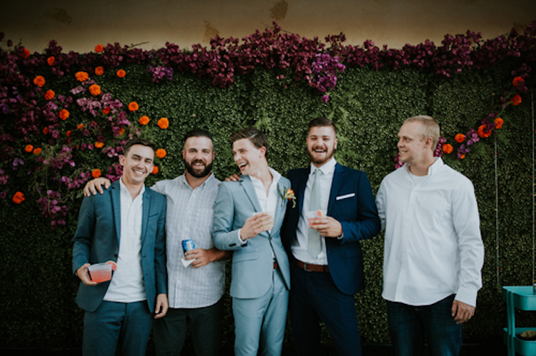 groom and groomsmen posing against a grass wall backdrop