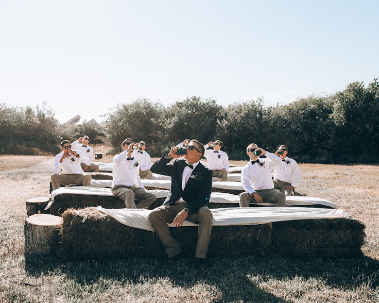 groom and groomsmen sitting and drinking in hay bale wedding ceremony seats