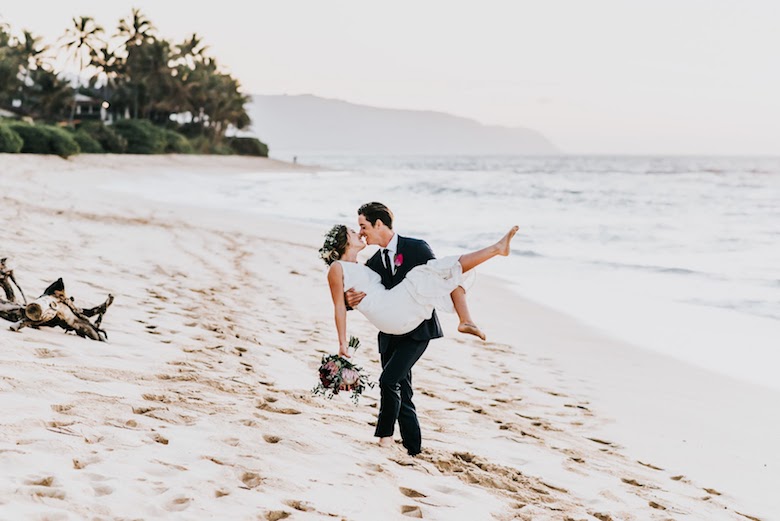 bohemian bride and groom kissing while walking on the beach