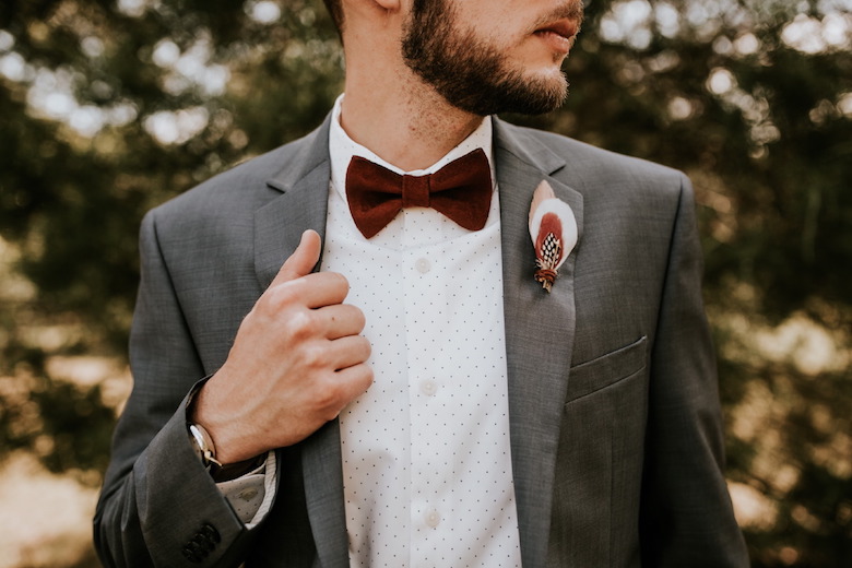groom wearing a gray suit, red bowtie, and a bohemian feather boutonniere 