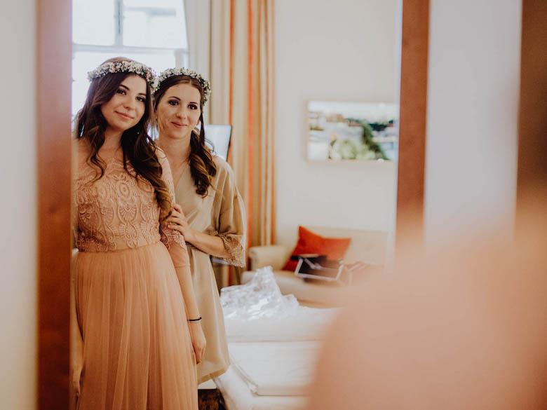 bride and bridesmaid looking into a mirror, smiling and happy. Day of the wedding