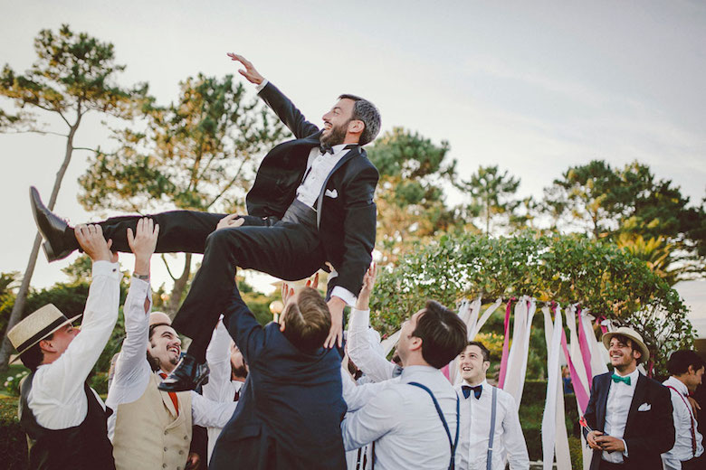 groom getting carried by the groomsmen, smiles all around, outdoor wedding with trees in the background