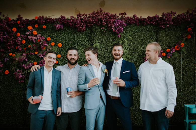 happy, laughing groomsmen standing in front of a red and green flower wall