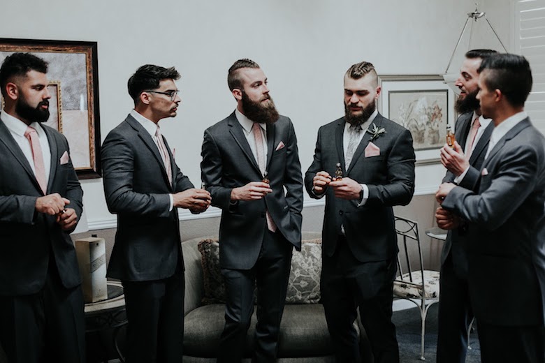 five groomsmen inside preparing to drink a mini bottle of liquor