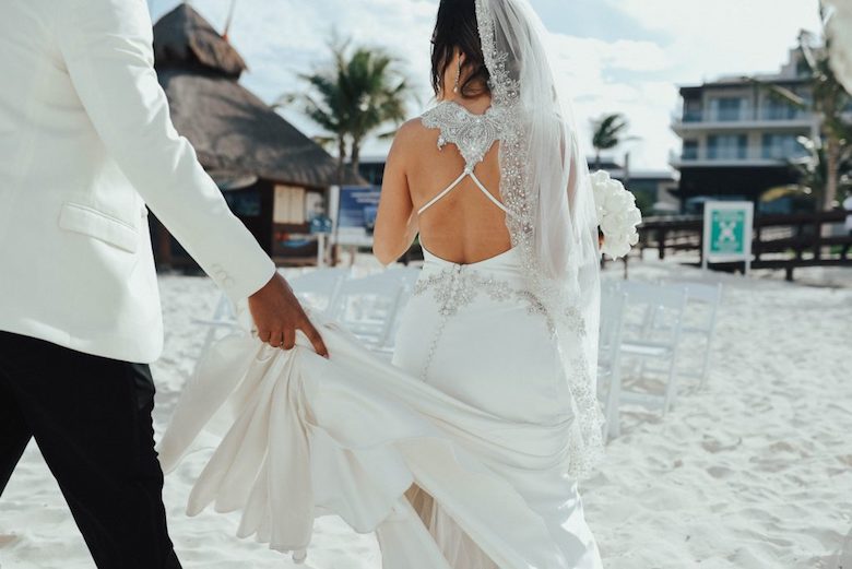 bride walking down the beach as her groom holds her train