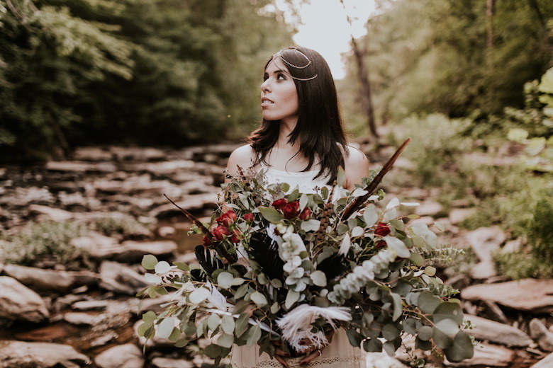 bride in the woods holding a wild bouquet of flowers