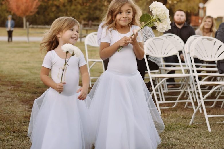 flower girls carrying big flower stems down the aisle at wedding