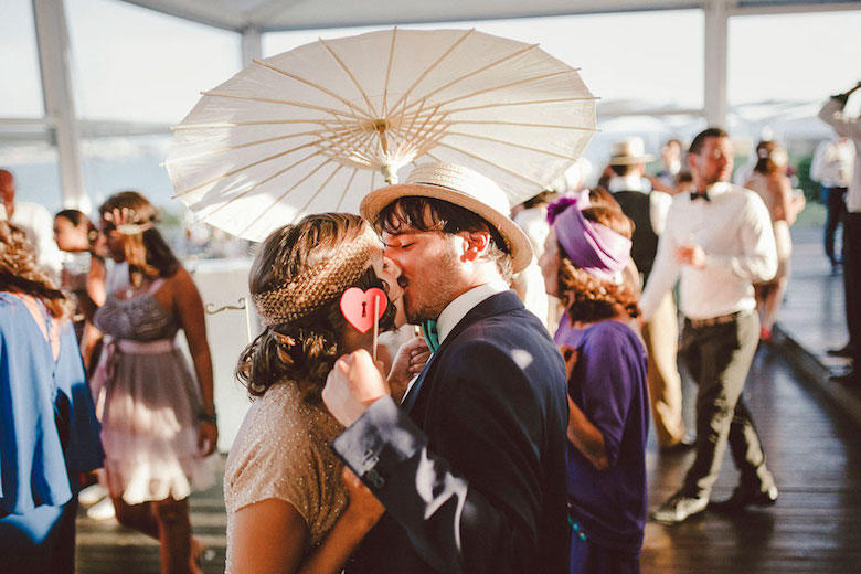 sunny outdoor wedding, groom and bride enjoy a kiss under a paper parasol