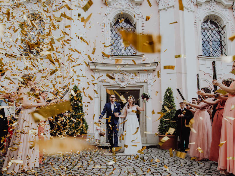 recently married couple walking out of venue into a shower of golden paper