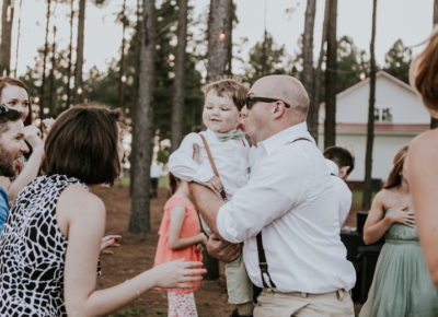 bald wedding guest wearing sunglasses playing with child