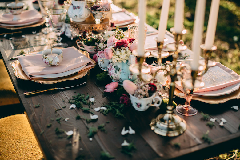 rose petals and sprigs scattered on whimsical wedding table settings 