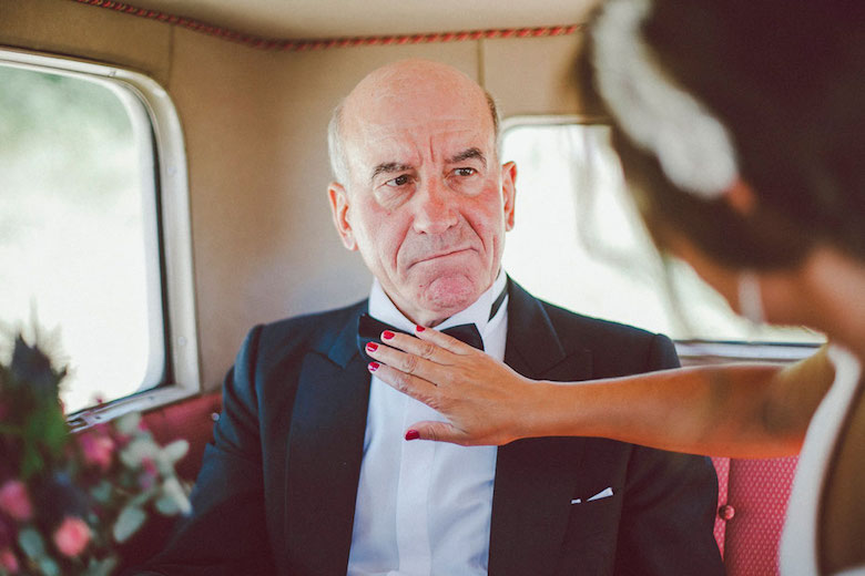 father of the bride getting his bowtie adjusted by his daughter, he looks stern but happy