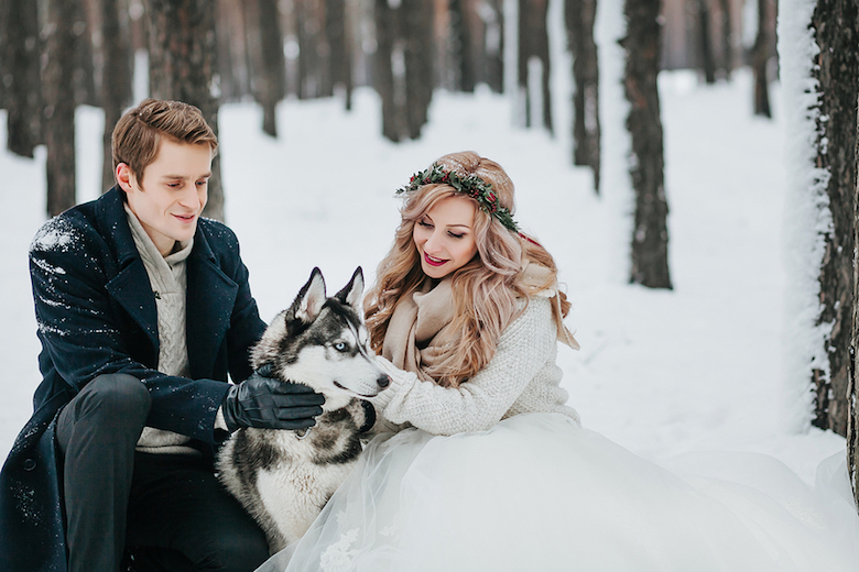 bride and groom sitting with husky in a snowy forest