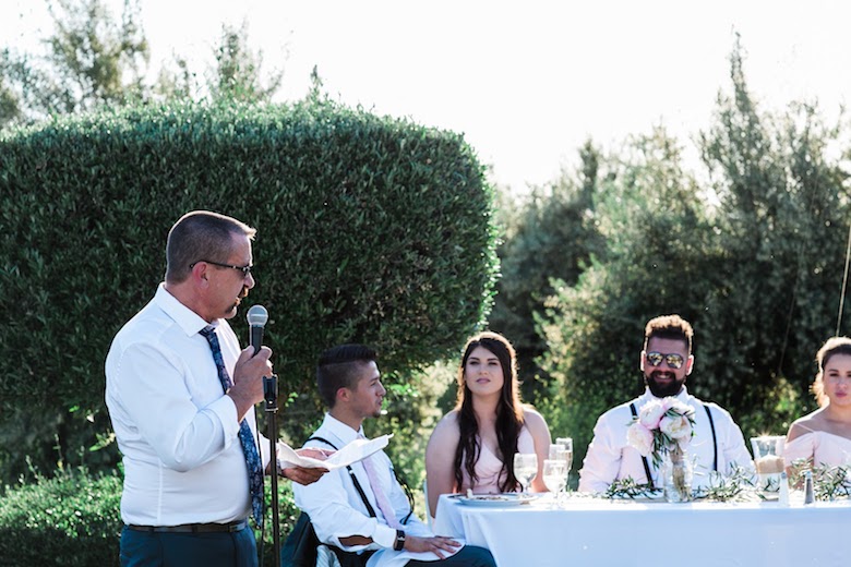 father giving a speech at an outdoor wedding, probably joking about his daughter or son